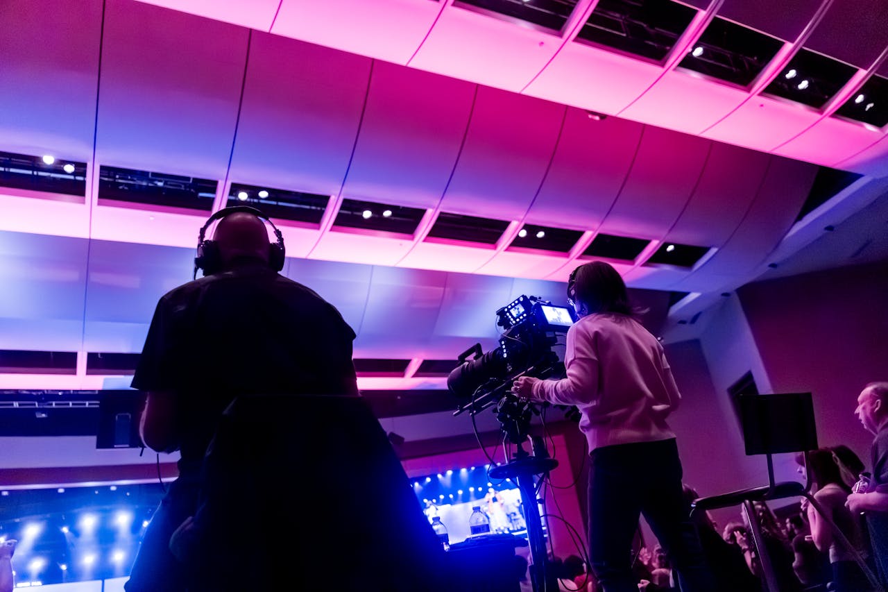 home-hero-bg Professional camera crew filming a live event indoors, capturing vibrant stage lighting.